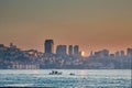 Fishing boats sail on the sea at dawn. City houses, skyscrapers in the light of the descending sun. Royalty Free Stock Photo